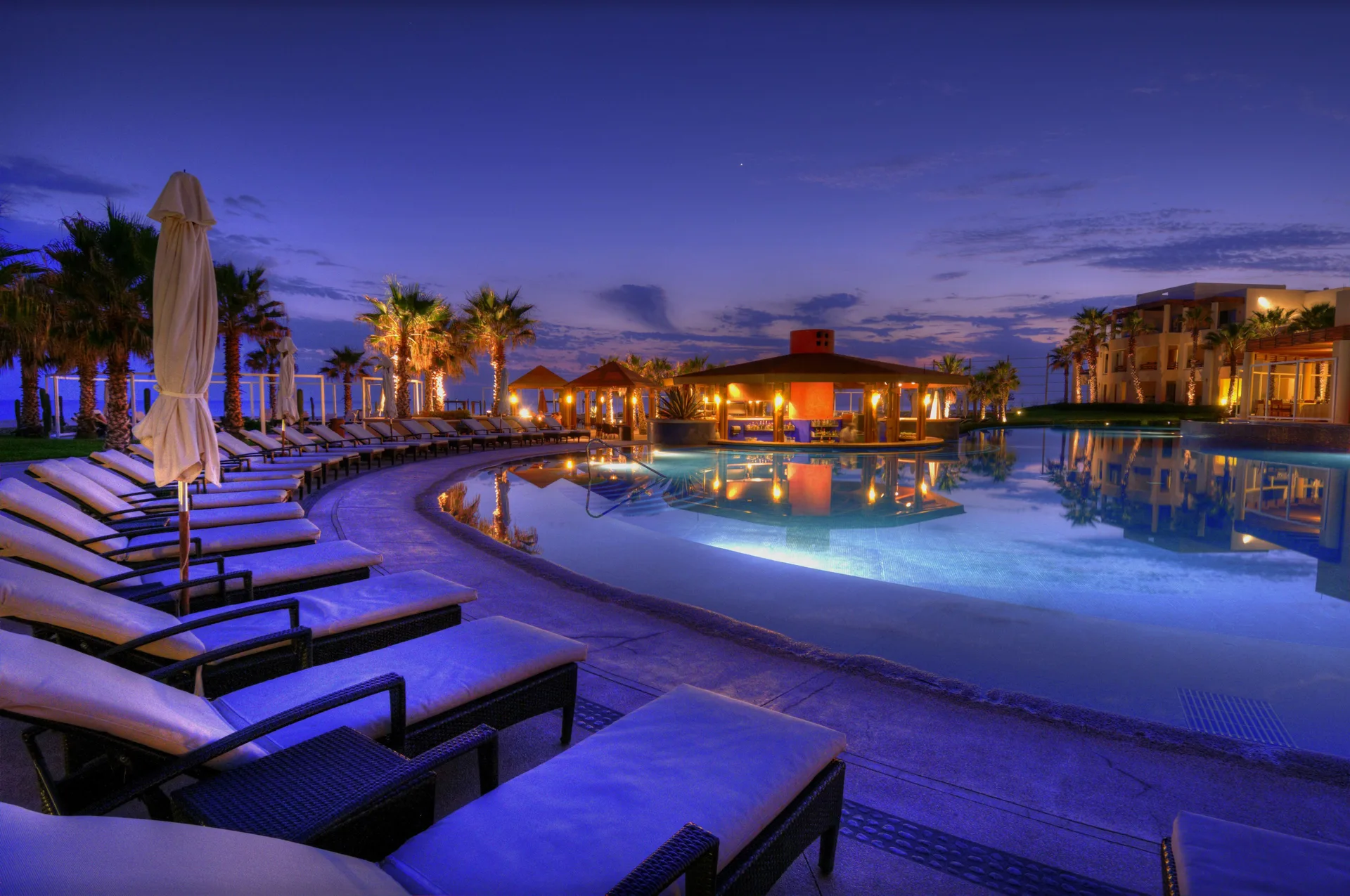 Twilight pool scene with loungers, palms, and warm pavilion lights at Pueblo Bonito Pacifica Golf & Spa Resort.