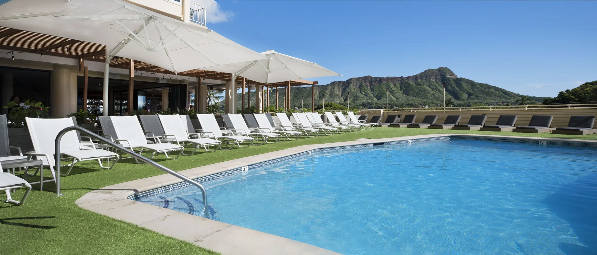 Curved pool edge with white loungers and Diamond Head at Queen Kapiolani Hotel.