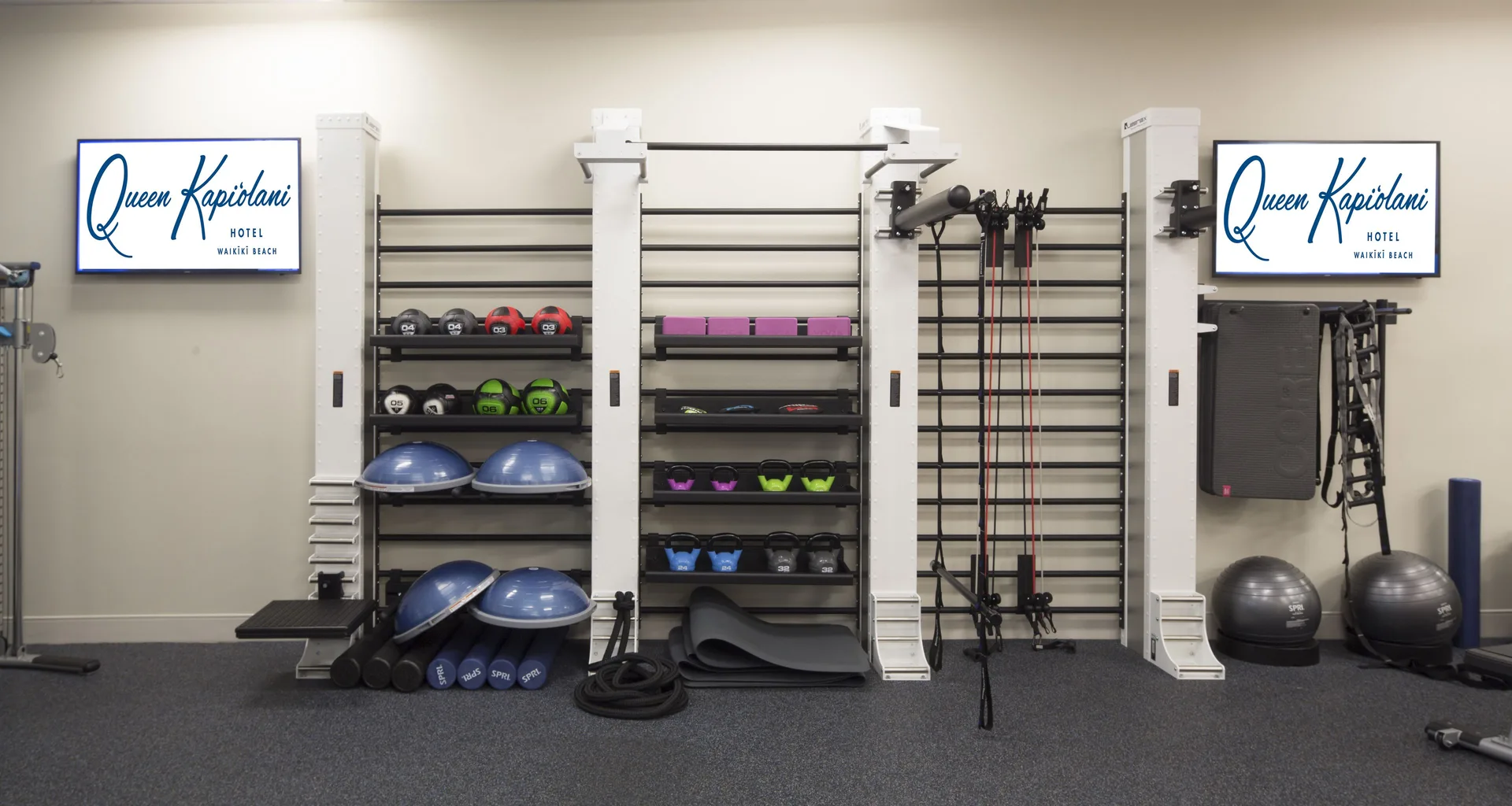 Fitness equipment is neatly organized on wall racks at Queen Kapiolani Hotel.