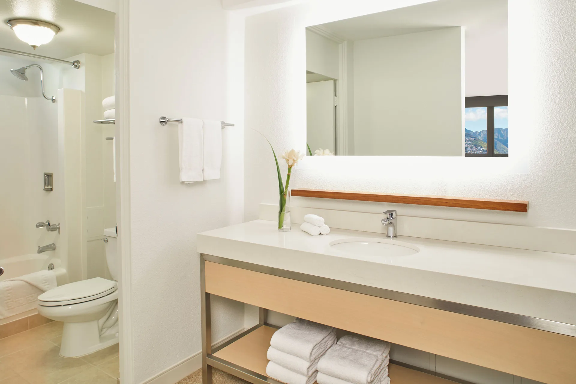 Bathroom vanity, mirror, shower, and towels in a guest room at Queen Kapiolani Hotel.