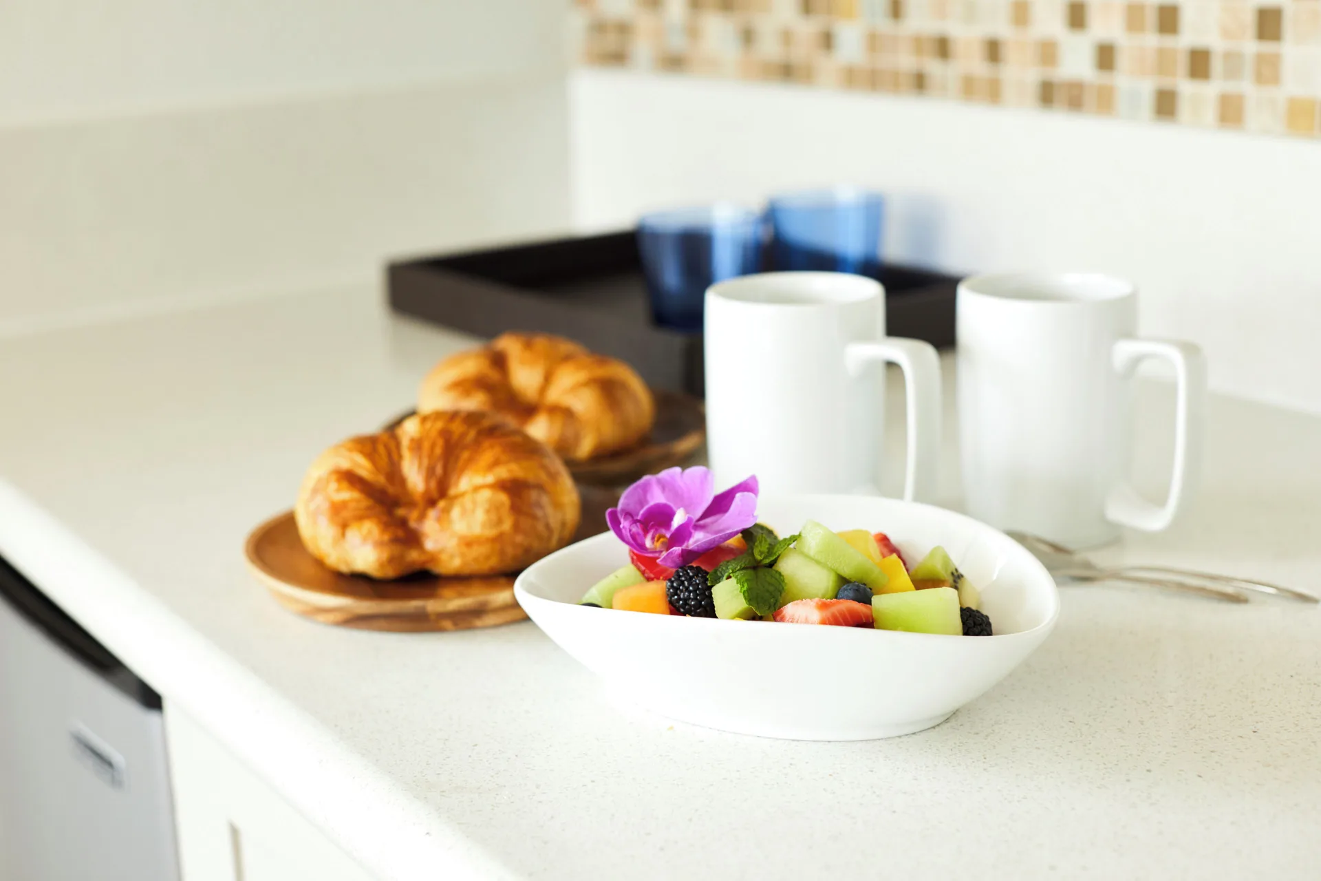 Fruit, croissants, and coffee mugs on a counter at Queen Kapiolani Hotel.