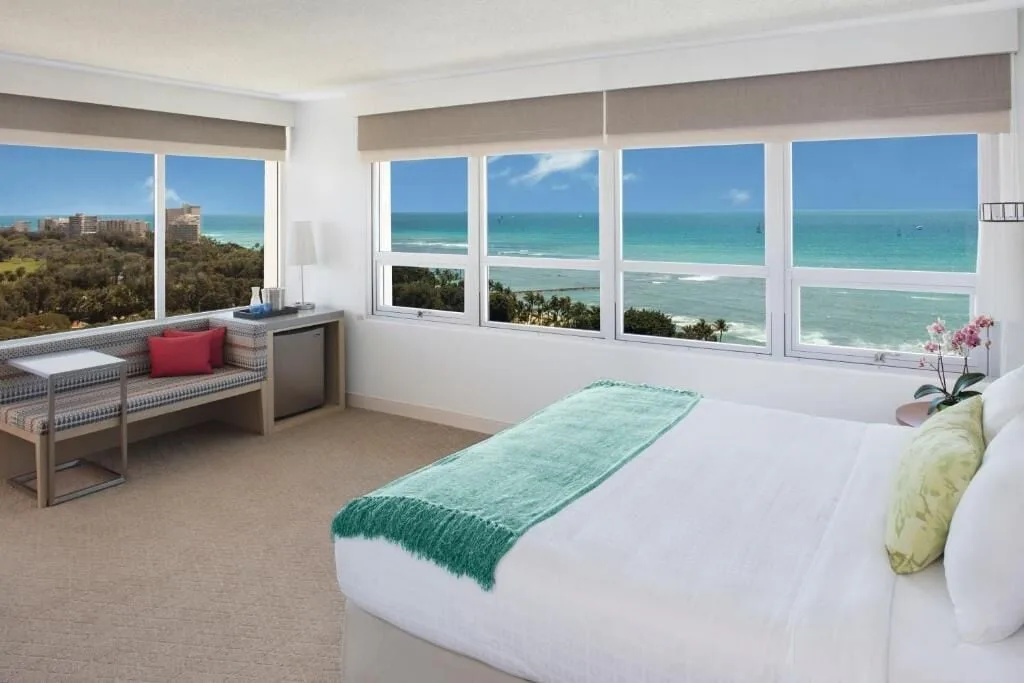 An ocean-view king guest room with wide windows at Queen Kapiolani Hotel.