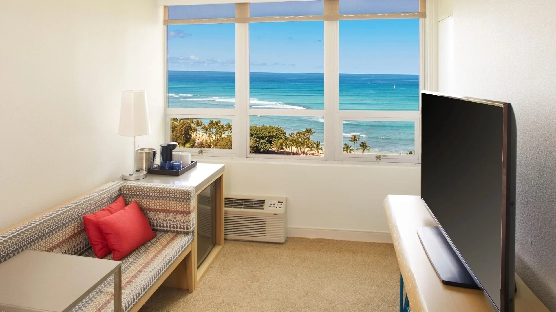A seating nook, television, and ocean view in a guest room at Queen Kapiolani Hotel.
