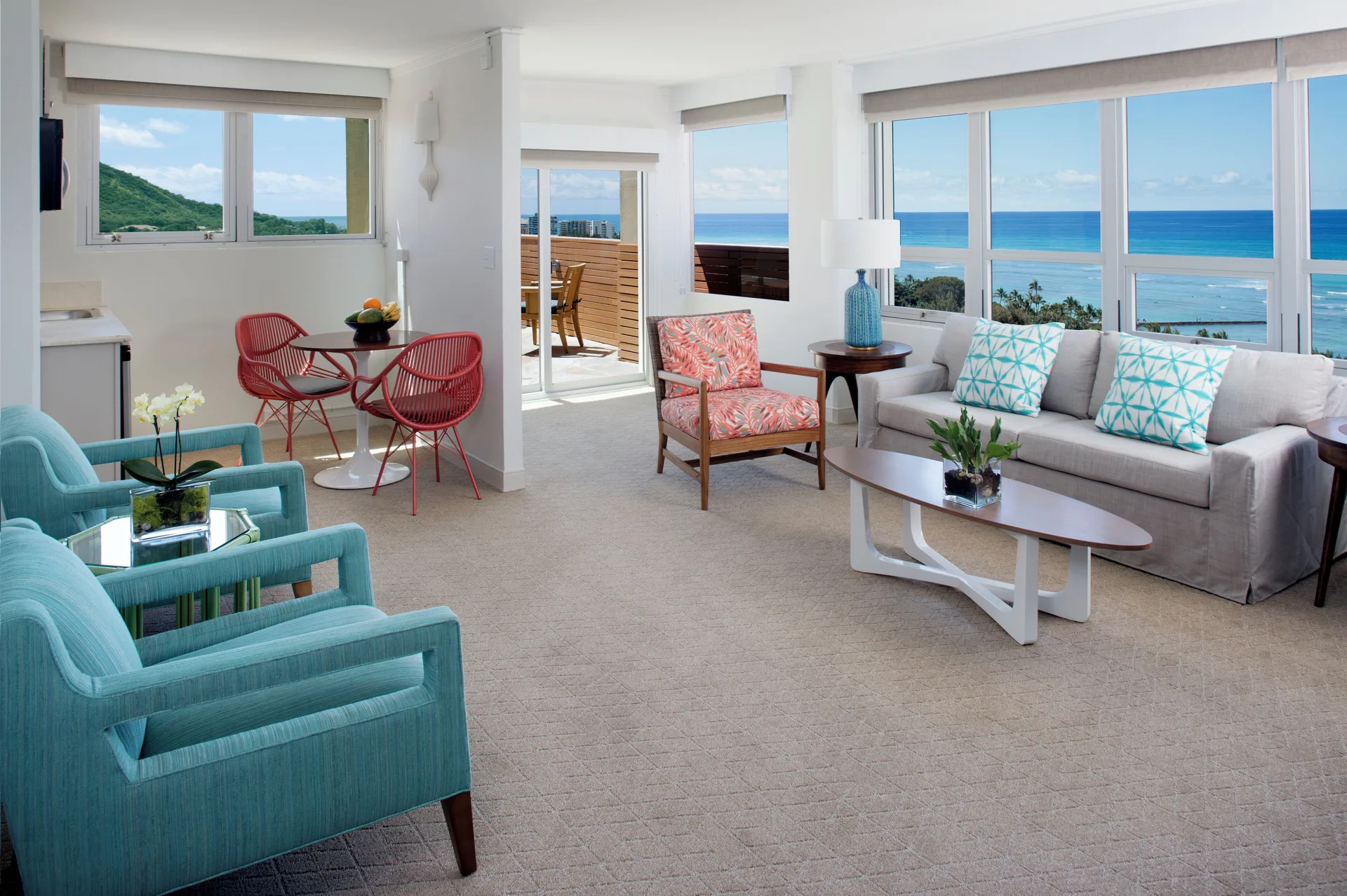 Bright ocean-view suite living room with balcony seating at Queen Kapiolani Hotel.