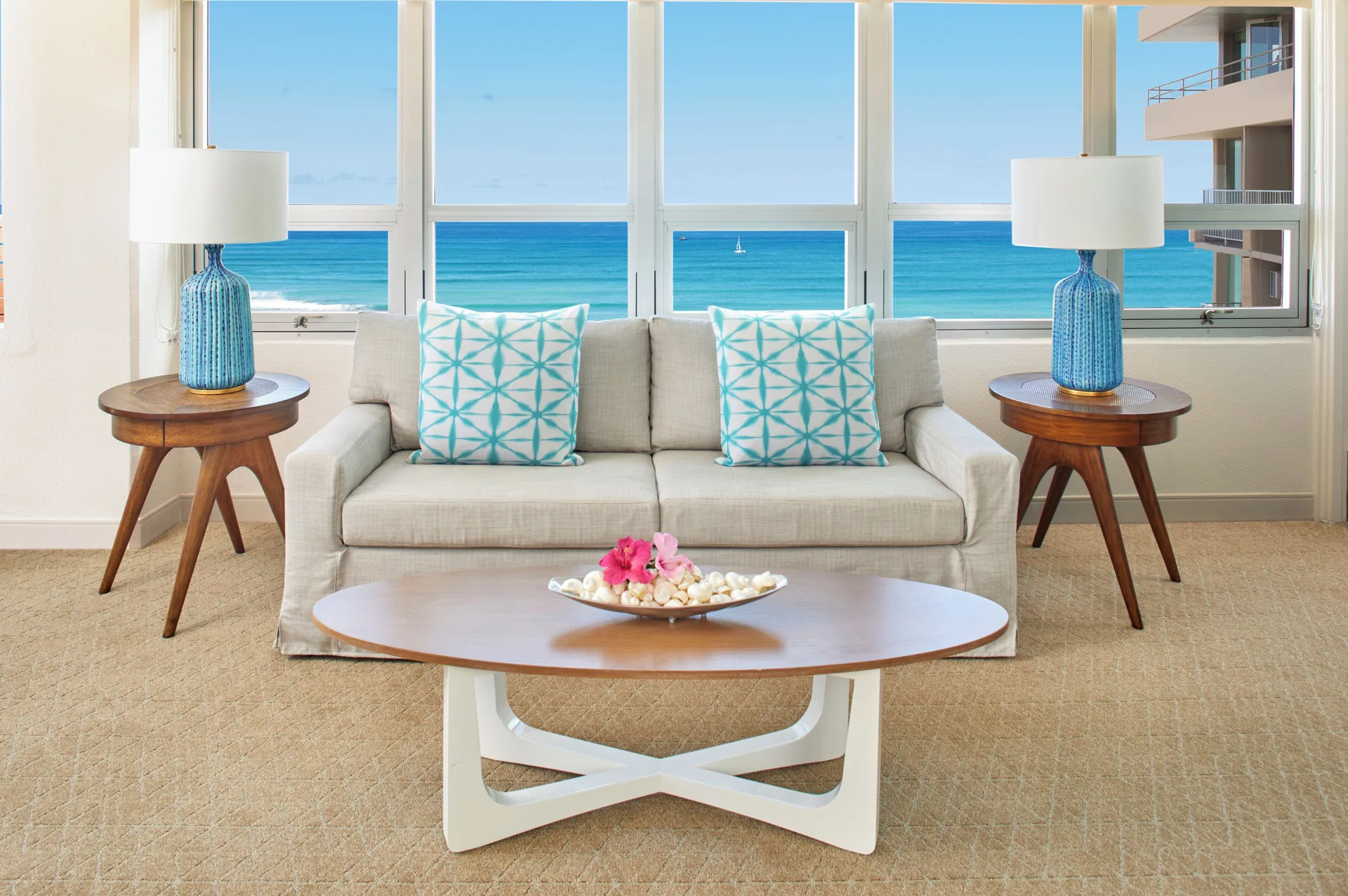 Sofa and side tables framed by large ocean-facing windows at Queen Kapiolani Hotel.