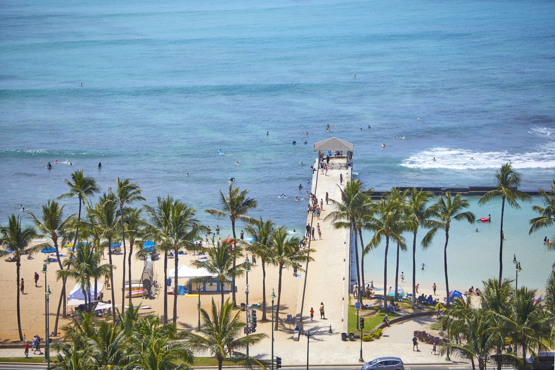 A pier, palms, beach, and ocean are seen from Queen Kapiolani Hotel.