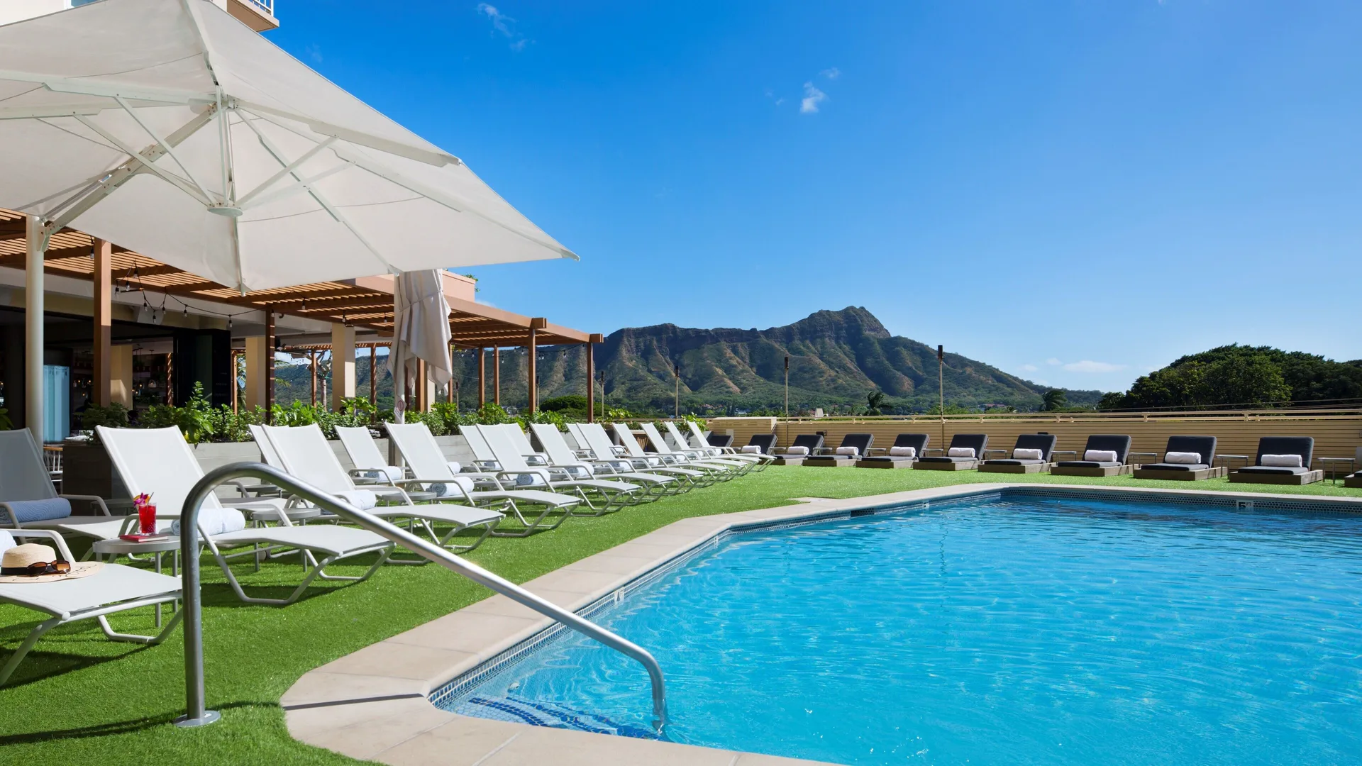 Pool with handrail, shaded loungers, and Diamond Head at Queen Kapiolani Hotel.
