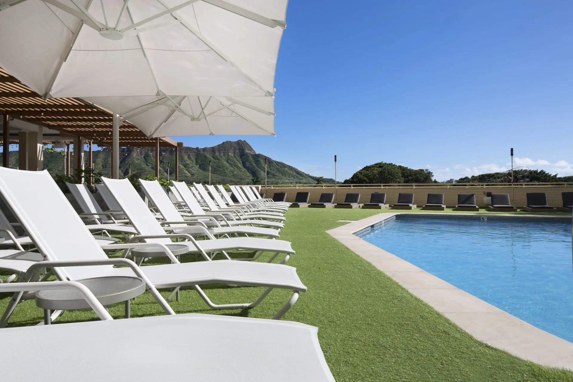 Poolside lounge chairs and umbrellas facing Diamond Head at Queen Kapiolani Hotel.