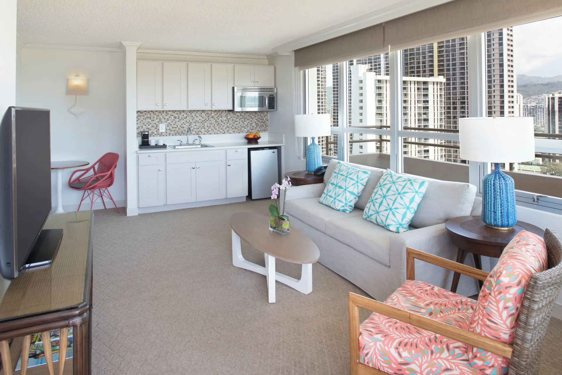 Suite living area with kitchenette, sofa, and city-view windows at Queen Kapiolani Hotel.