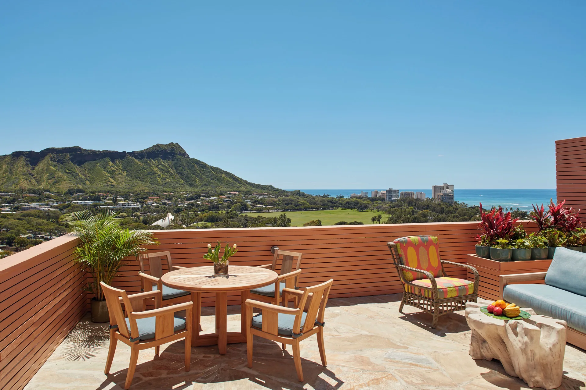 Sunlit terrace with seating, plants, Diamond Head, and ocean views at Queen Kapiolani Hotel.