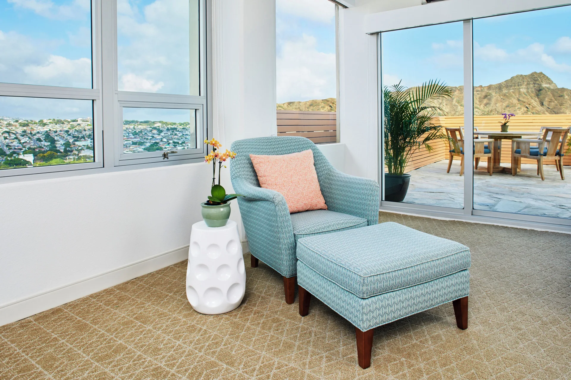 Blue armchair and ottoman beside windows and a terrace at Queen Kapiolani Hotel.