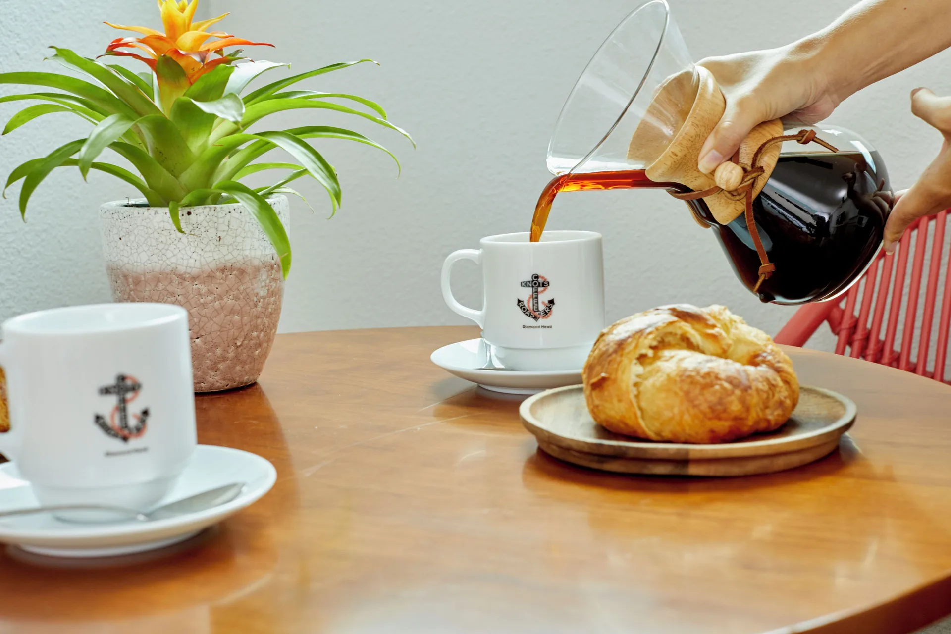 Coffee is poured beside mugs, a pastry, and a plant at Queen Kapiolani Hotel.