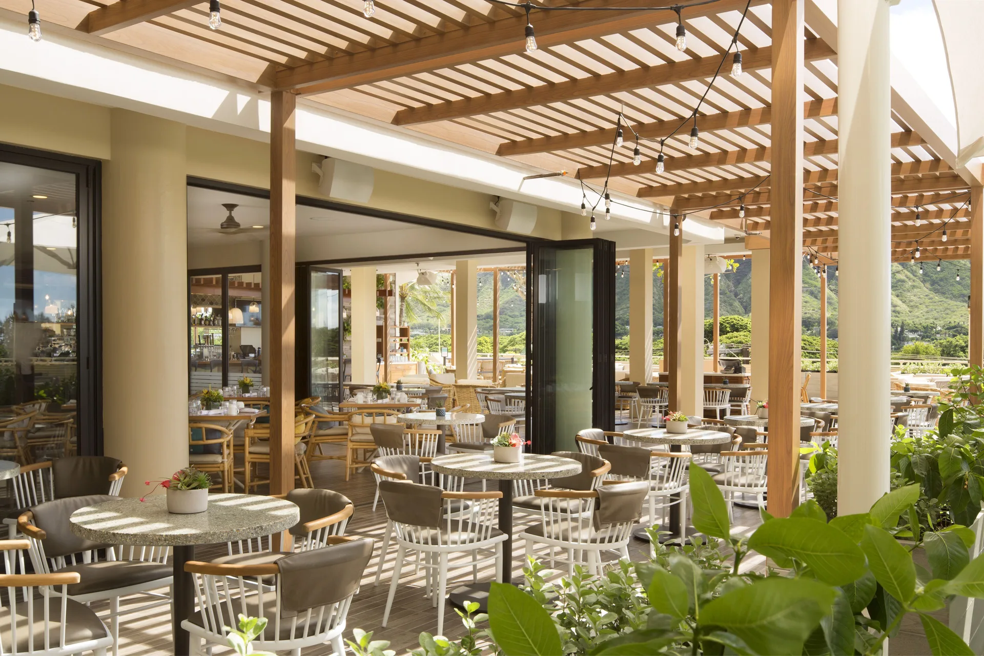 Open-air restaurant patio with tables and mountain views at Queen Kapiolani Hotel.