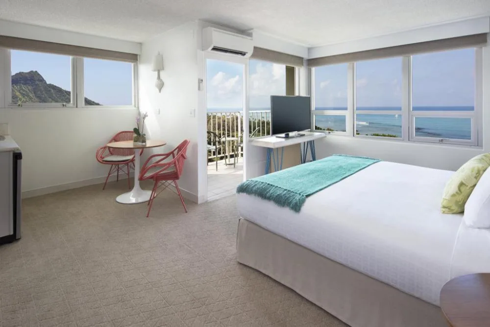 Junior Suite Ocean View bedroom with king bed and ocean windows at Queen Kapiolani Hotel.