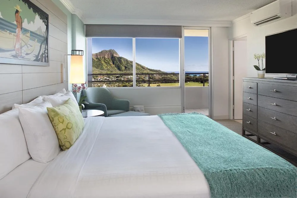 Penthouse One Bedroom Ocean View Suite bedroom with ocean and Diamond Head views at Queen Kapiolani Hotel.