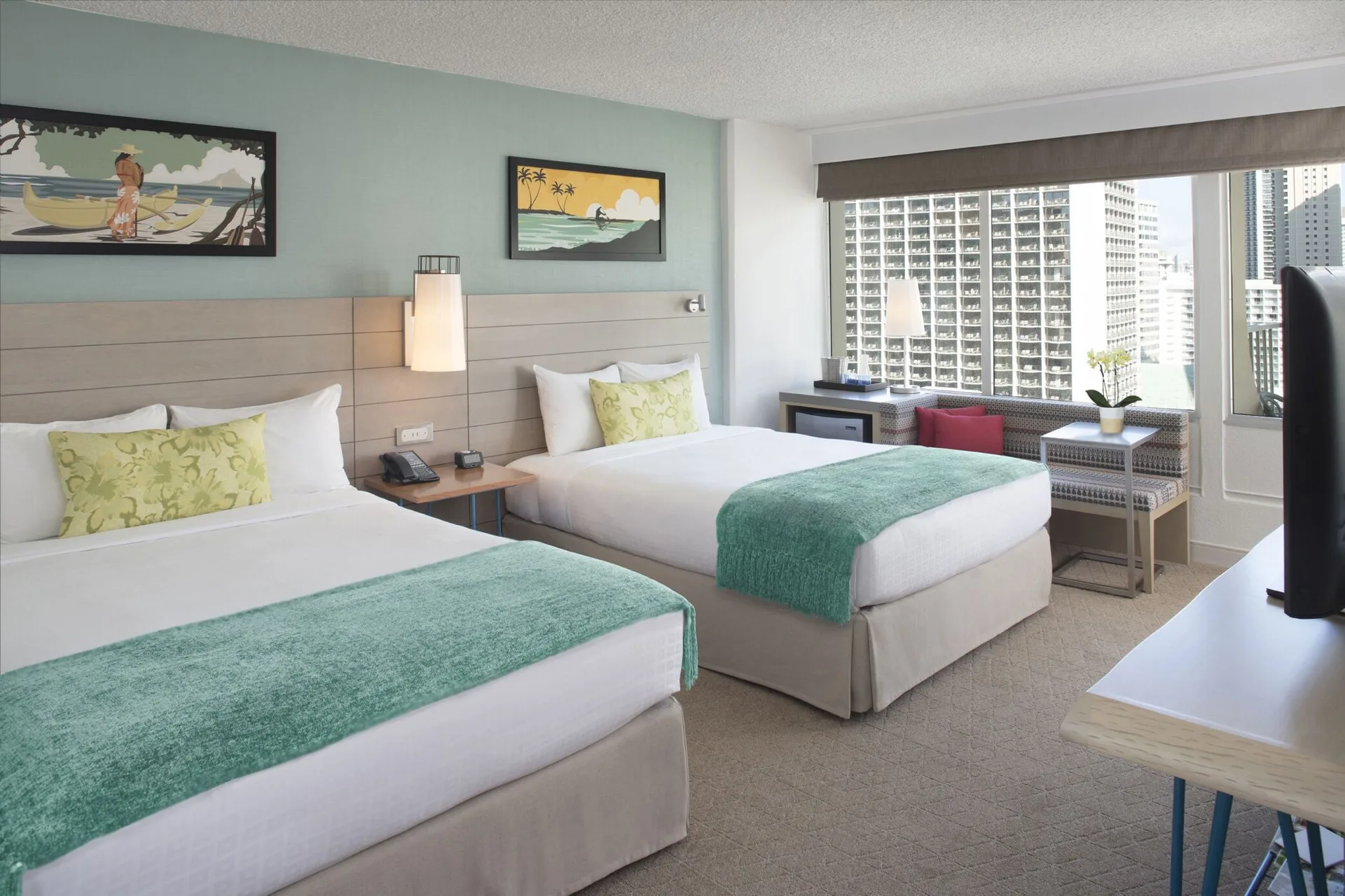 Two-bed city view room with desk and window seating at Queen Kapiolani Hotel.