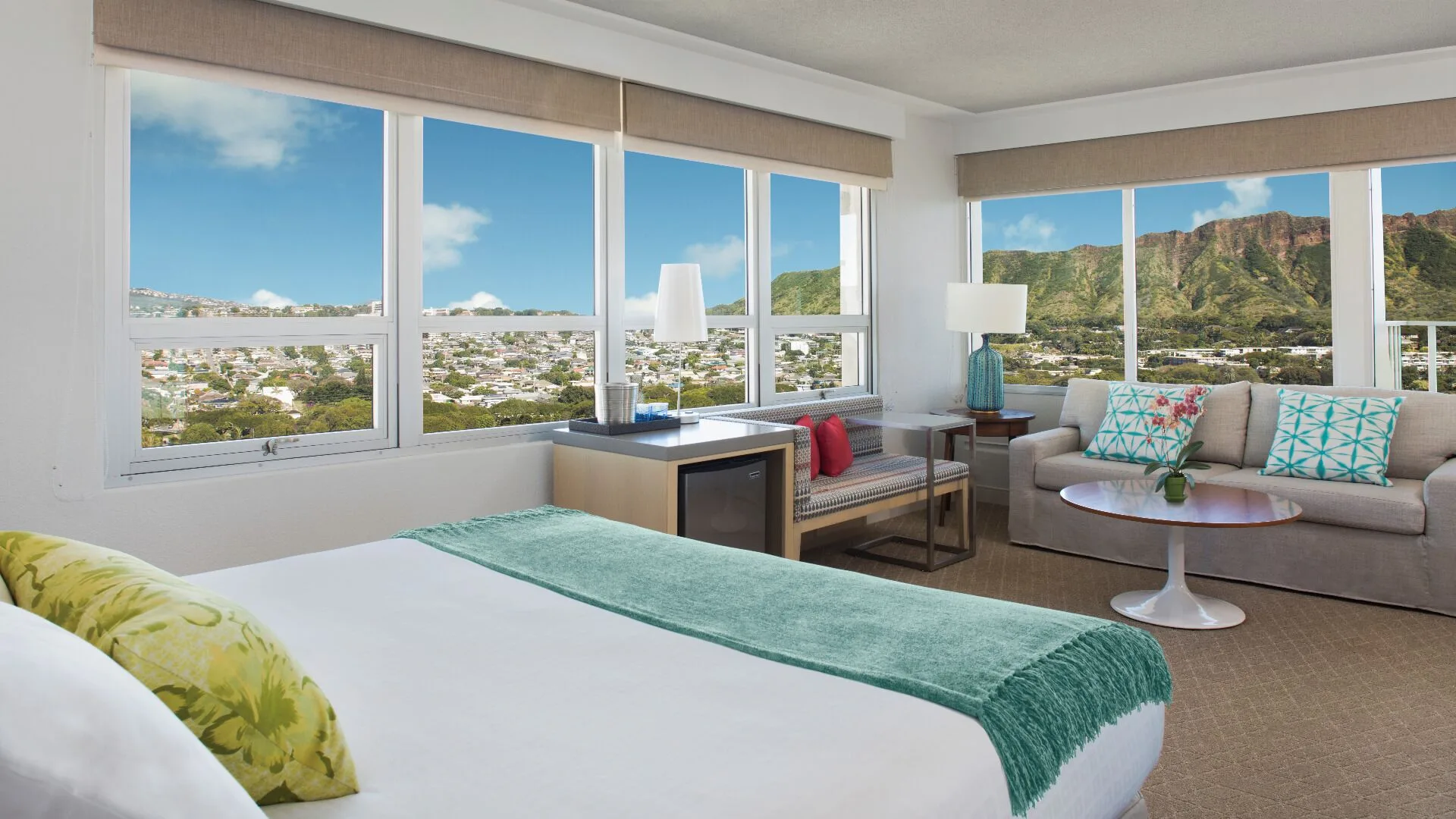 Diamond Head view guest room at Queen Kapiolani Hotel with a bed, sofa, and wraparound windows.