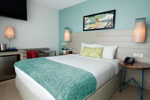Studio king room with teal throw, wall art, TV, and side table at Queen Kapiolani Hotel.