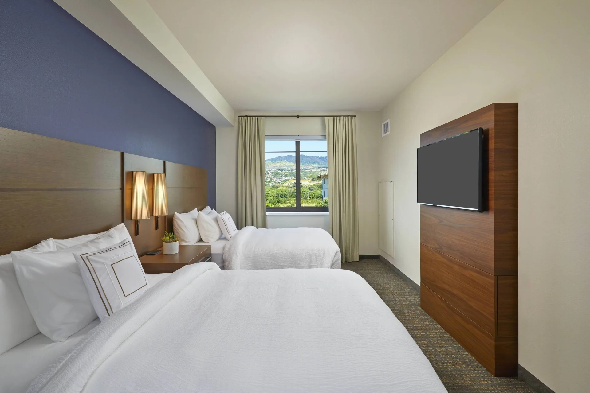 One-bedroom suite sleeping area with two beds and wall-mounted TV at Residence Inn Oahu Kapolei.