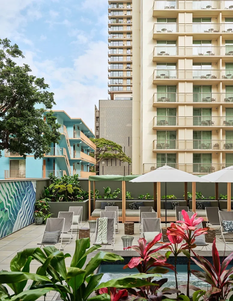 Pool deck with loungers, umbrellas, and city buildings at Romer House Waikiki.