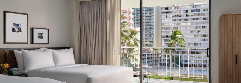 Deluxe Two Queens ADA room at Romer House Waikiki with balcony and city-facing windows.