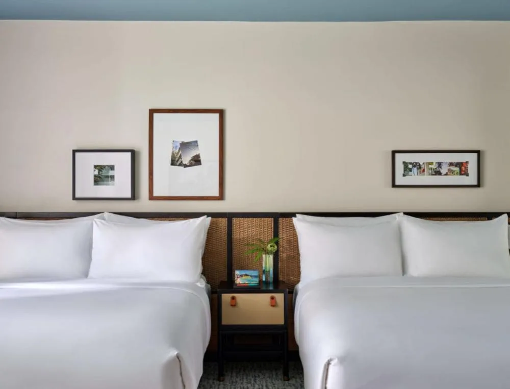Deluxe Two Queens ADA room at Romer House Waikiki with two white queen beds and framed wall art.
