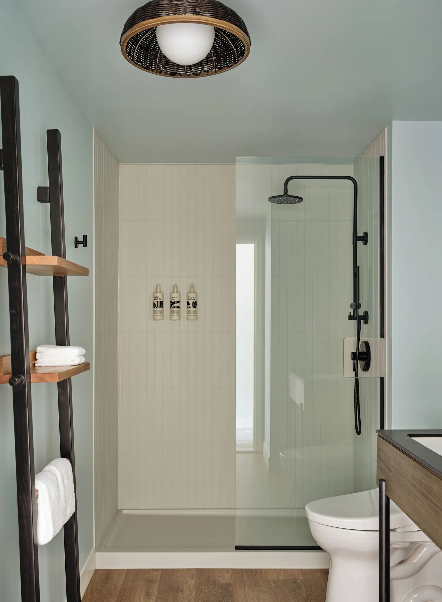 Bathroom with glass shower, black fixtures and towel shelving at Romer House Waikiki.