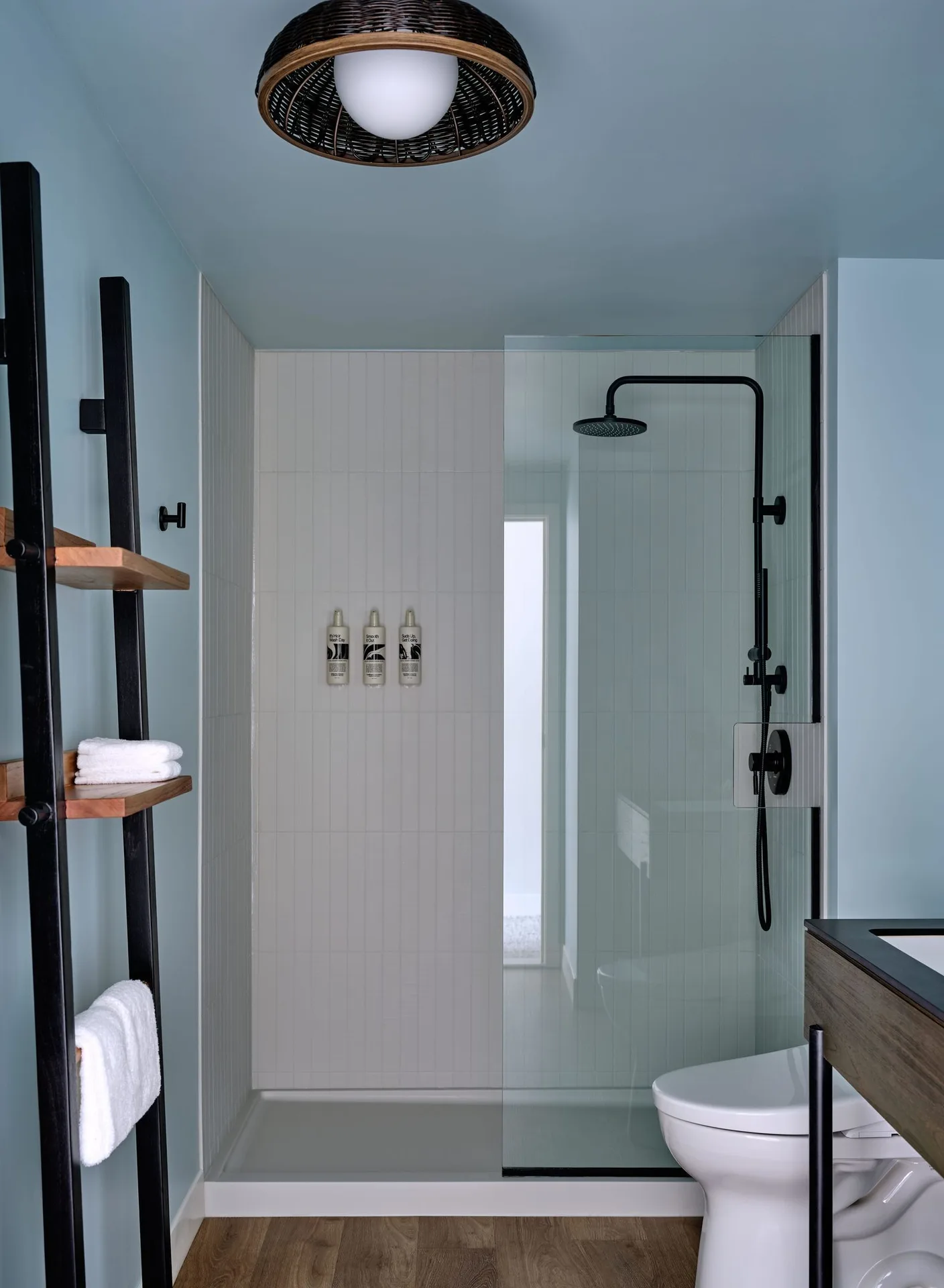 Standard Room bathroom with glass shower and wood shelving at Romer House Waikiki.