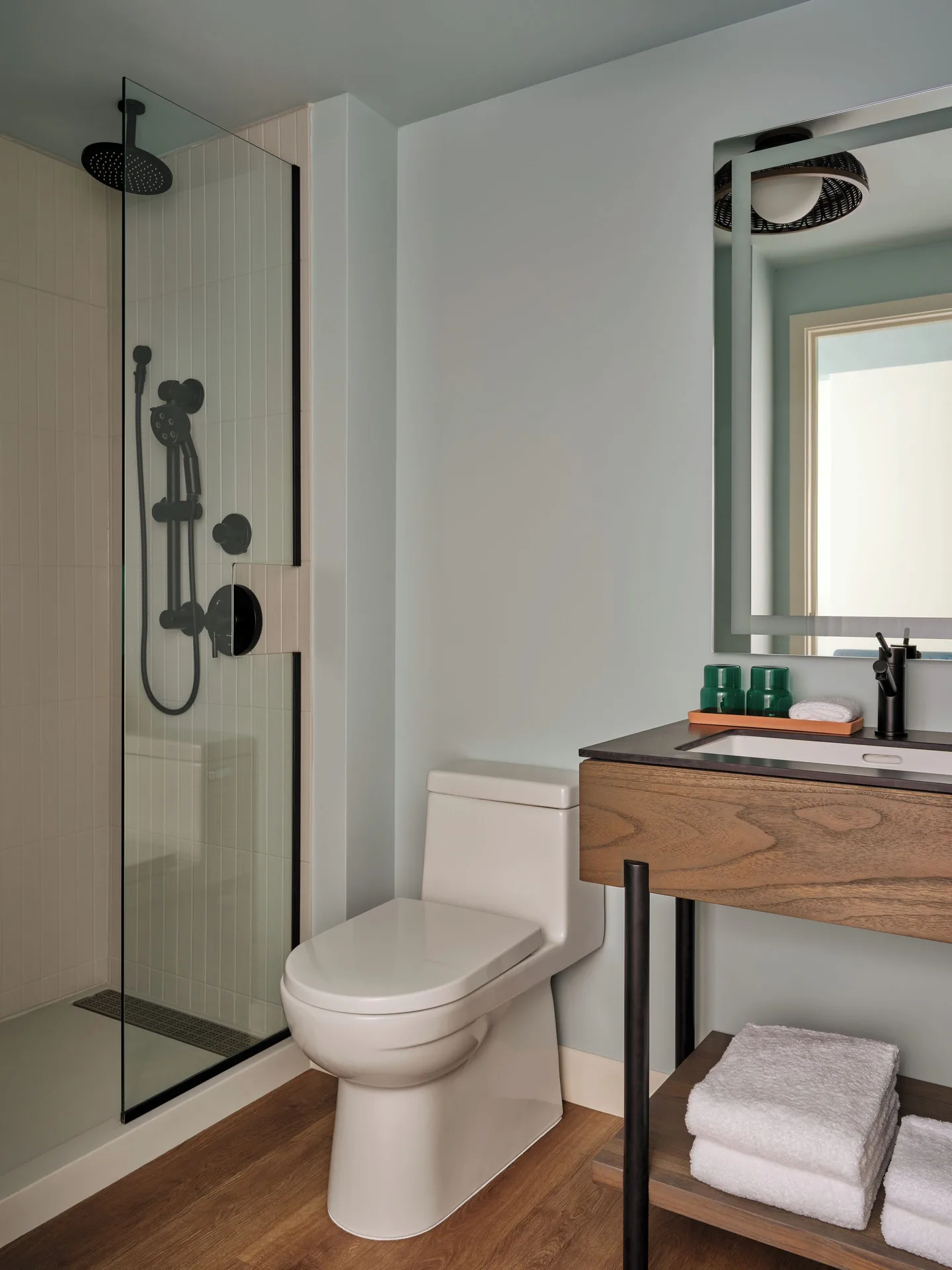 Standard room bathroom at Romer House Waikiki with glass shower, toilet, vanity, and folded towels.