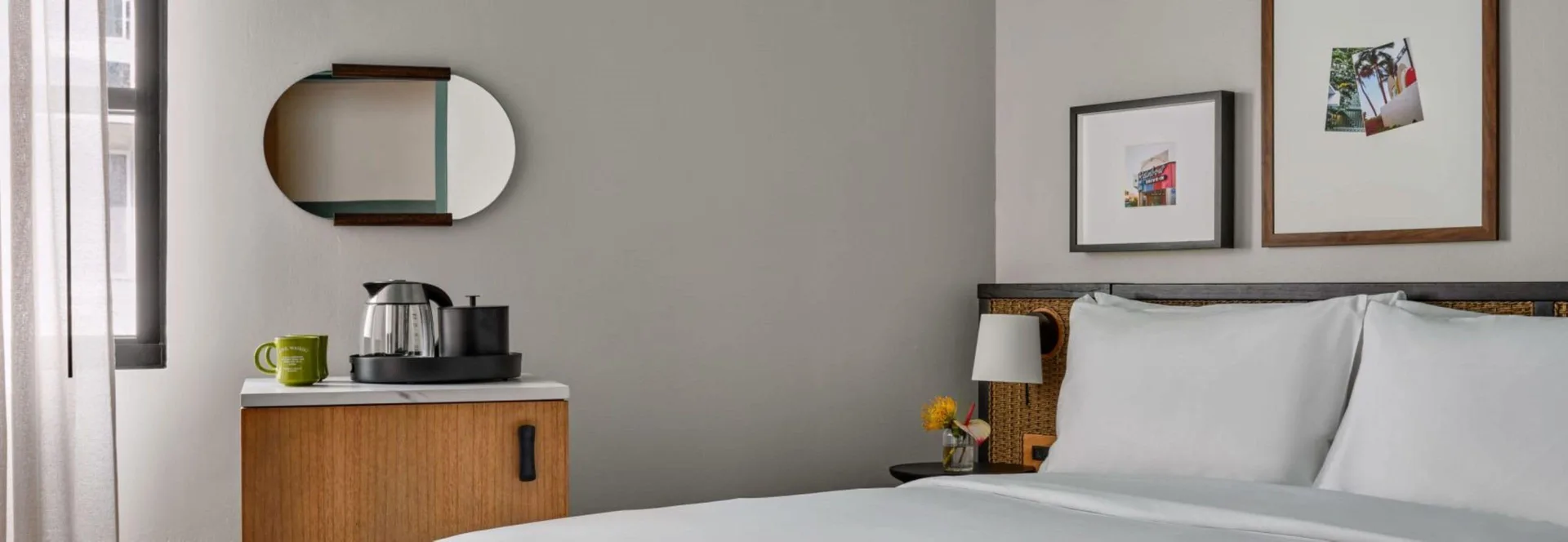 Standard room king bed at Romer House Waikiki with coffee cabinet, wall mirror, artwork, and bedside lamp.