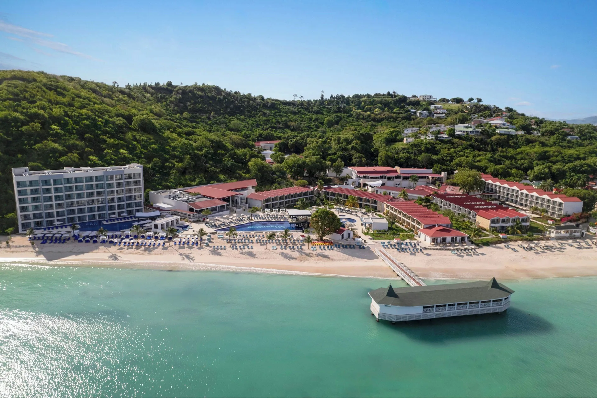 Aerial view of Royalton CHIC Antigua beachfront resort, pools, hillside, and overwater building.