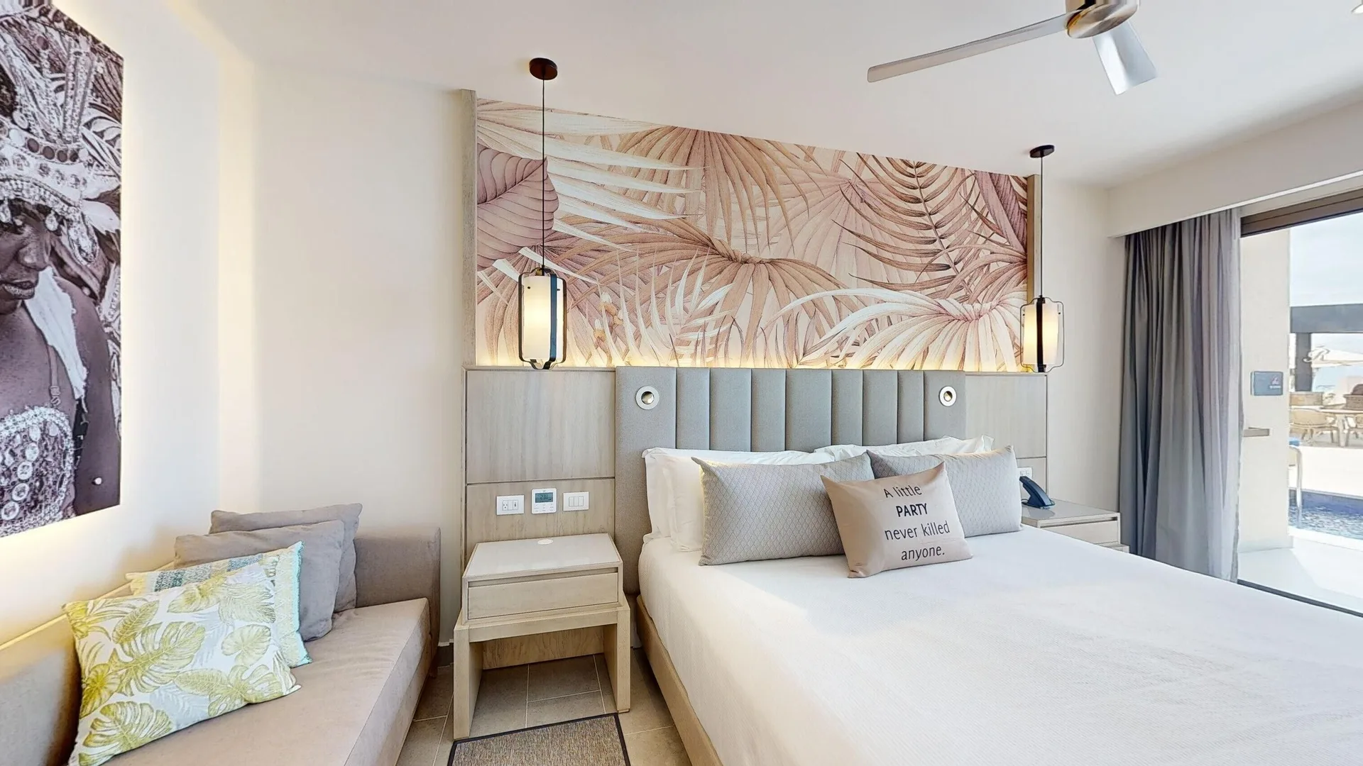 King bed with tropical wall art and sofa beside swim-out terrace at Royalton CHIC Antigua.
