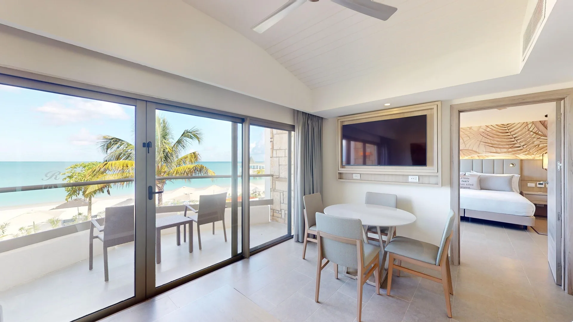 Suite living room with dining table, TV, balcony, and bedroom at Royalton CHIC Antigua.