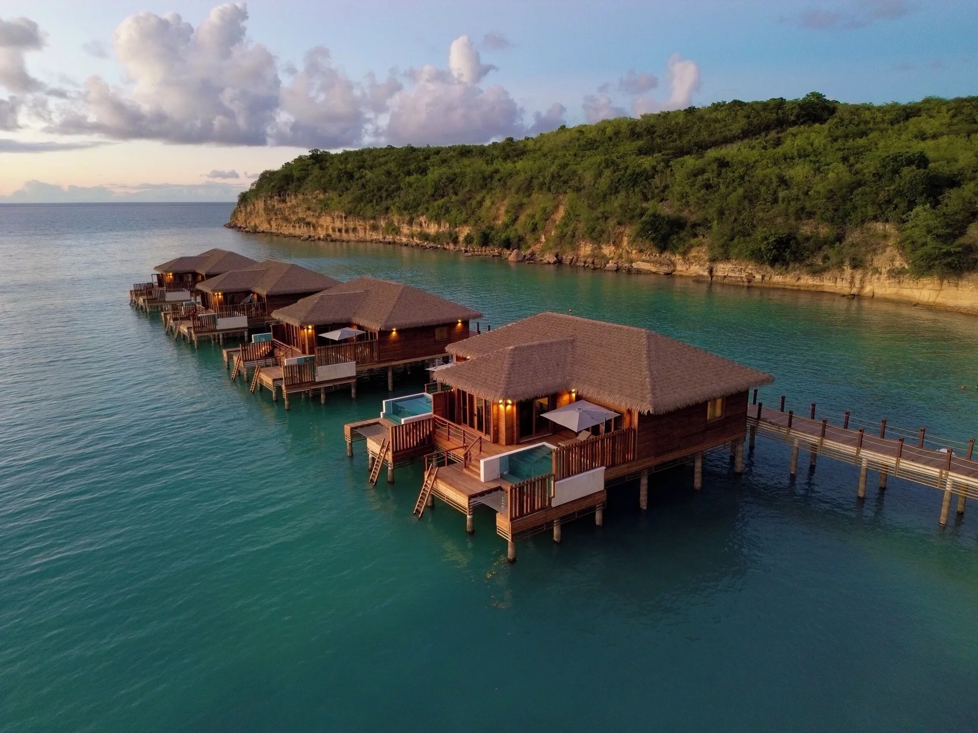 Overwater suites on turquoise water at Royalton CHIC Antigua, with private decks beside a green headland.