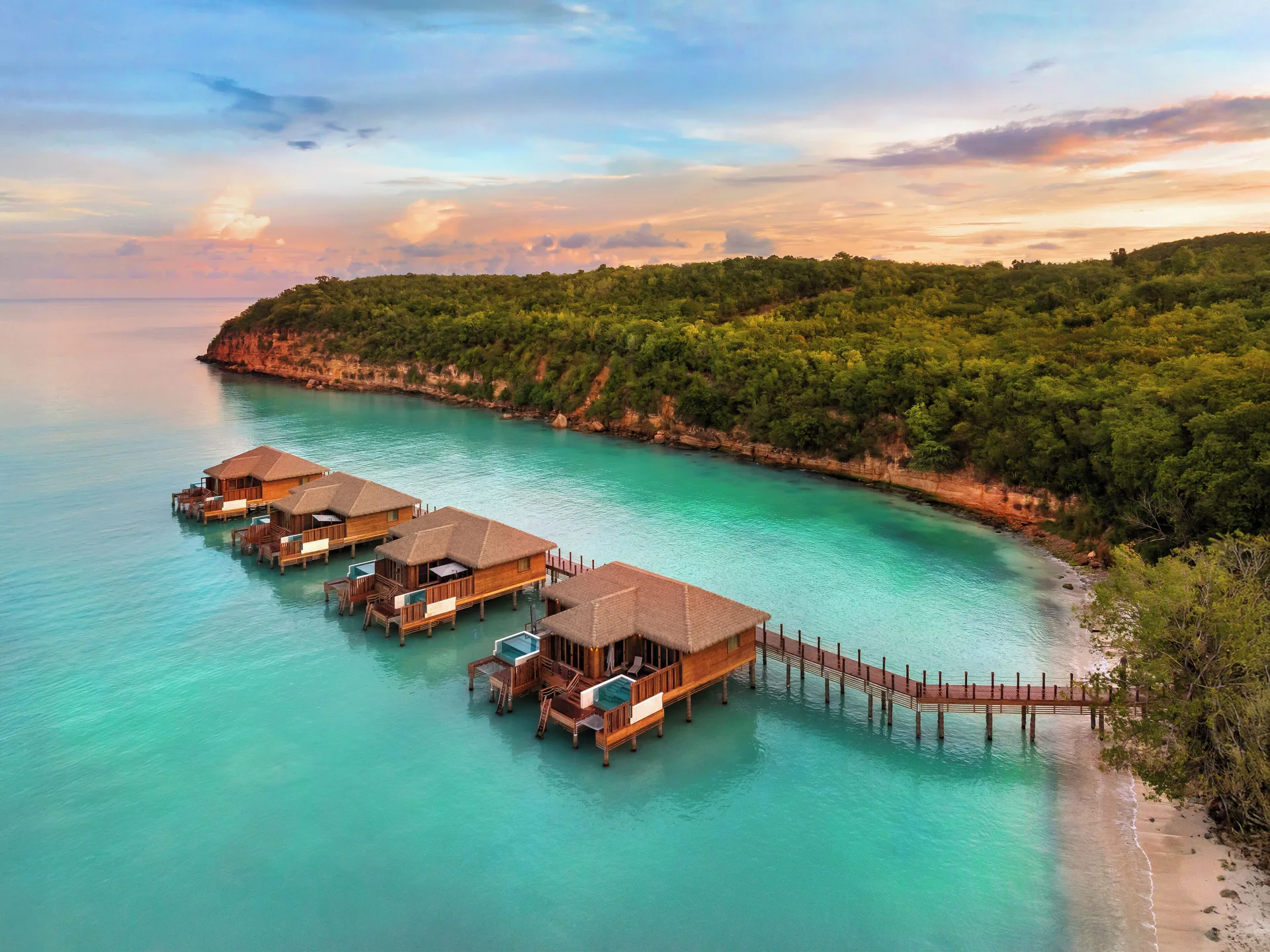 Sunset aerial of overwater suites and turquoise bay at Royalton CHIC Antigua.