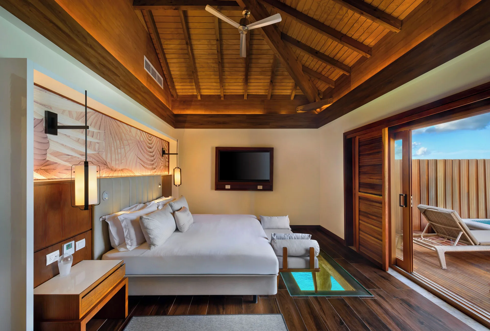King bed in an overwater suite at Royalton CHIC Antigua with a glass floor panel and deck doors.