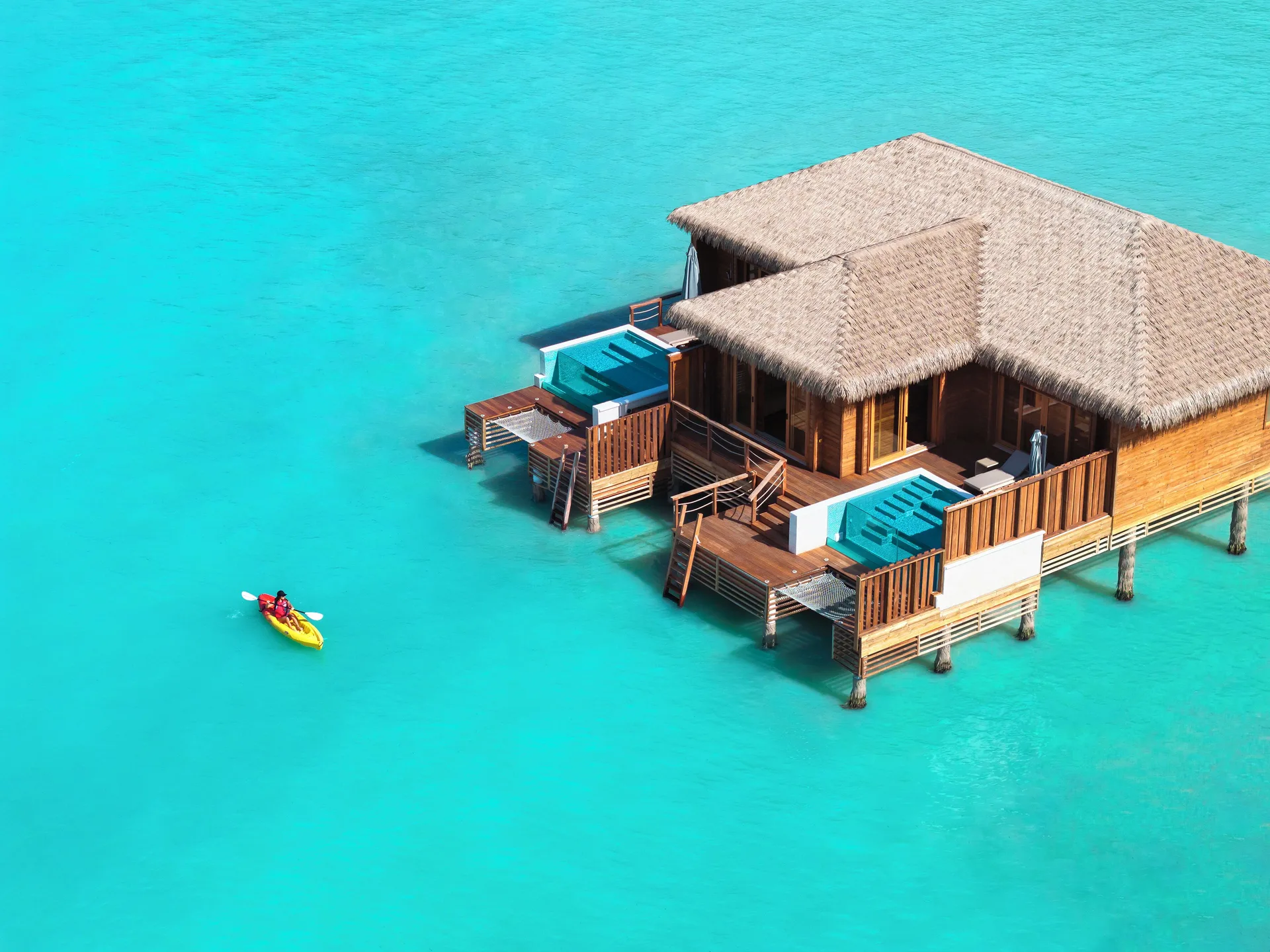 Overwater suite at Royalton CHIC Antigua with plunge pools and a kayak on bright turquoise water.