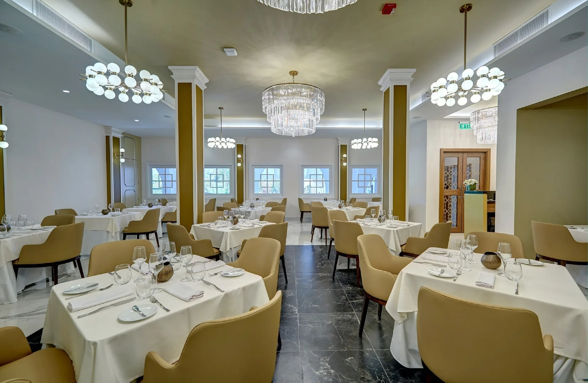 Elegant dining room at Royalton Grenada with white tablecloths, beige chairs, and chandeliers.