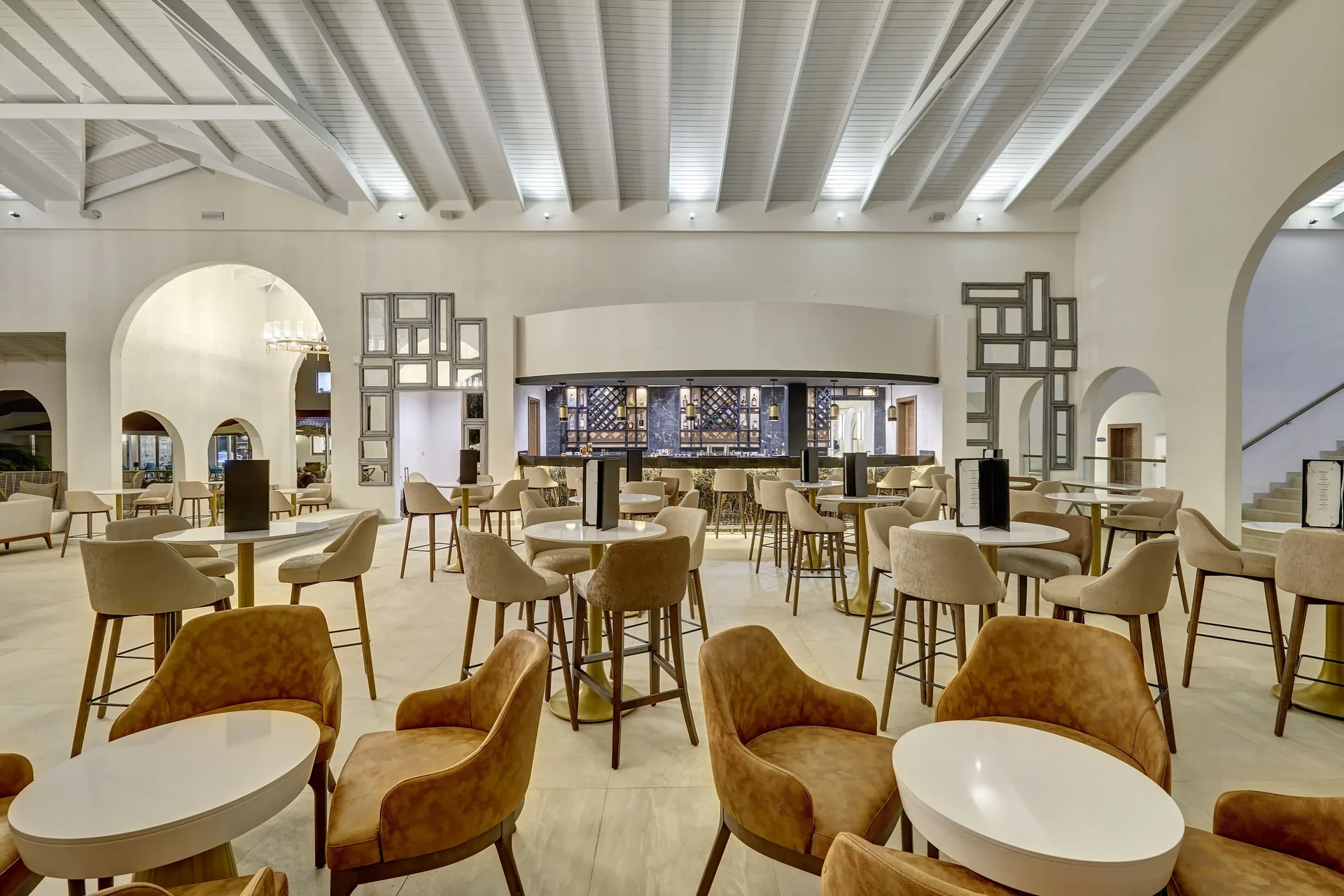 Lobby bar seating with round tables and a back bar at Royalton Grenada.