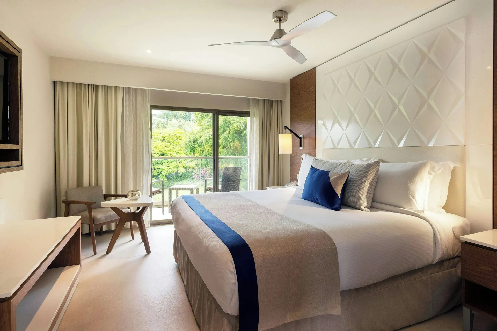 Luxury Room king bed at Royalton Grenada with balcony doors, seating area, and greenery outside.