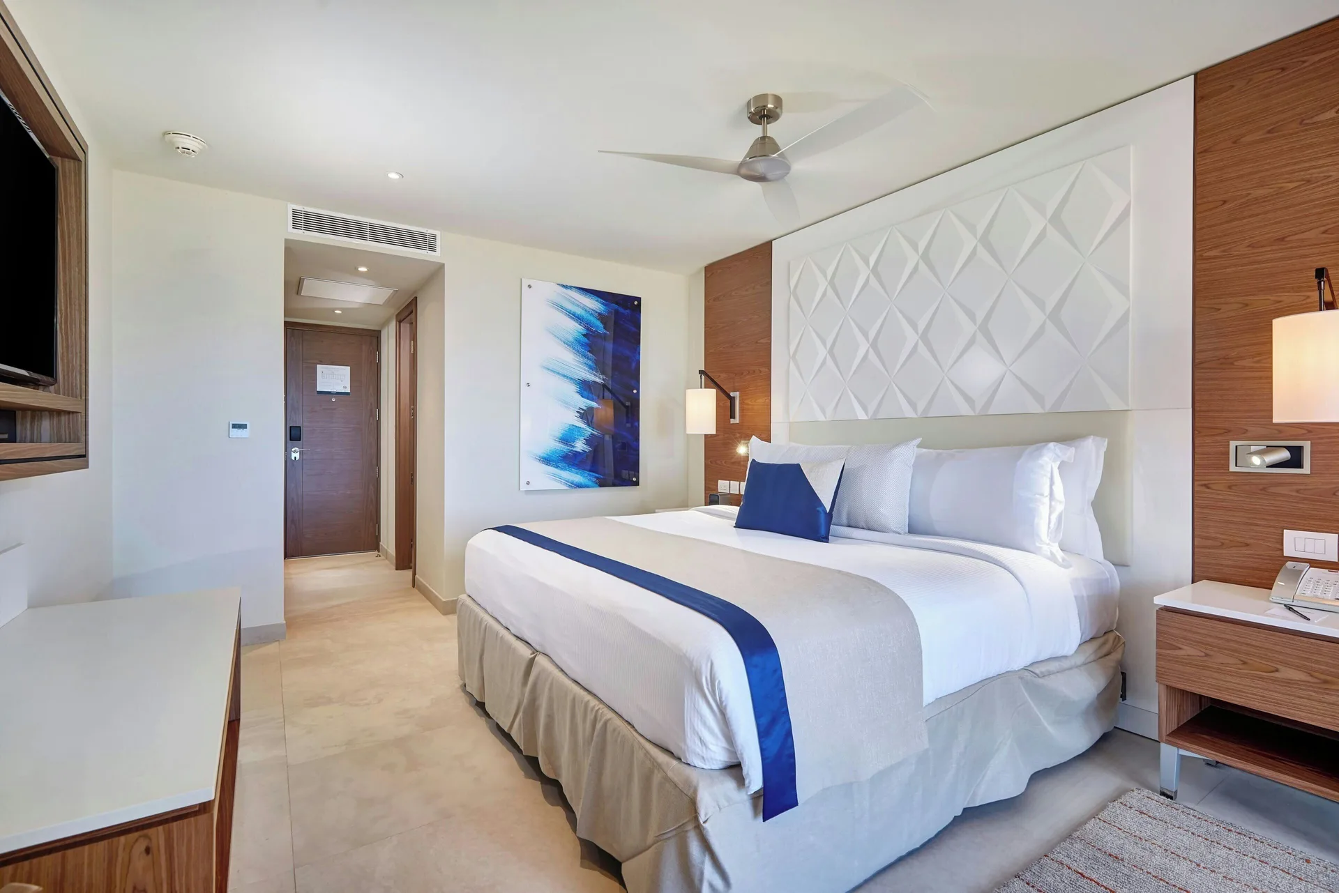 Luxury Room king bed at Royalton Grenada with blue accents, wall art, and bedside table.