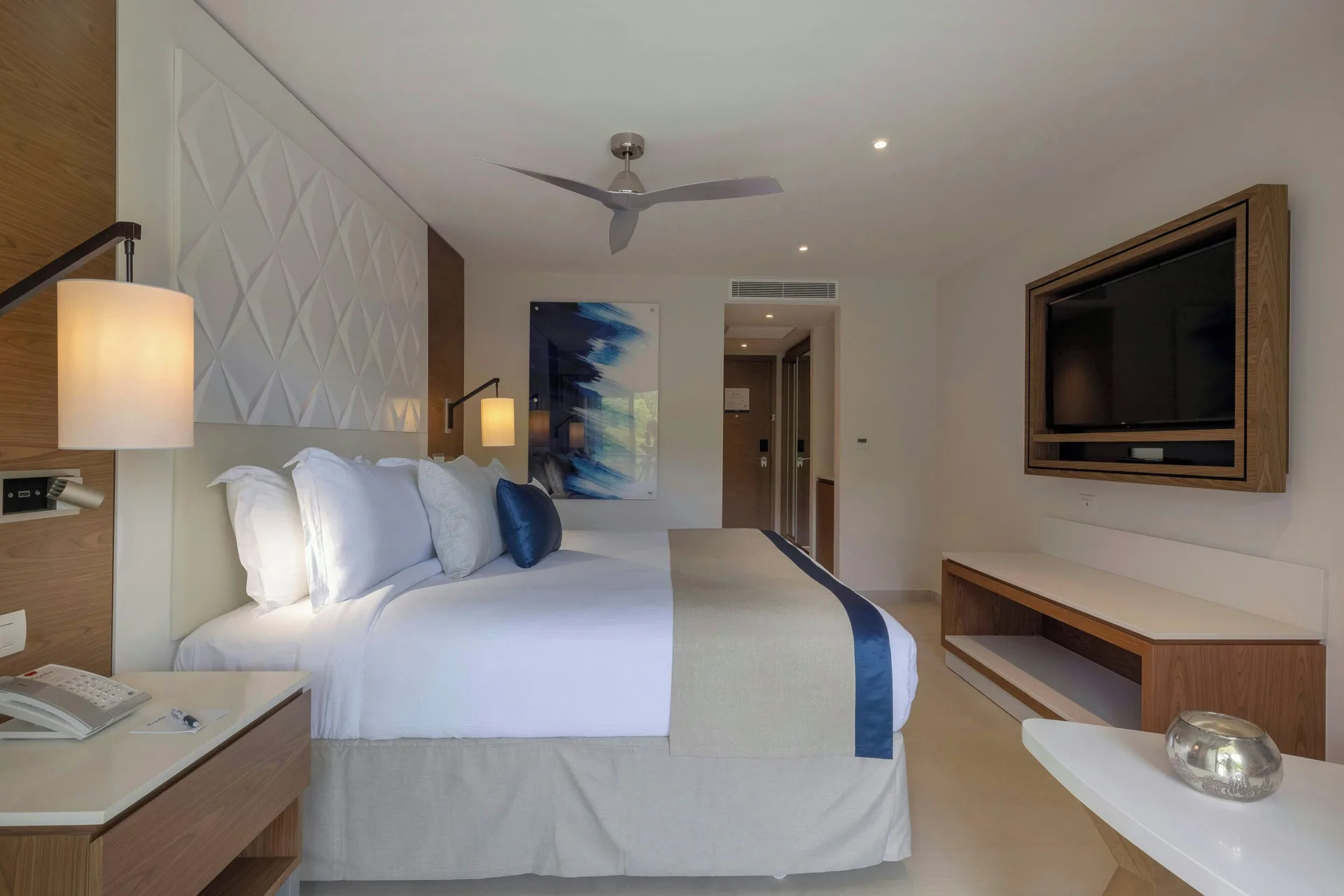 Luxury Room king bed at Royalton Grenada with wall-mounted TV, desk, and ceiling fan.