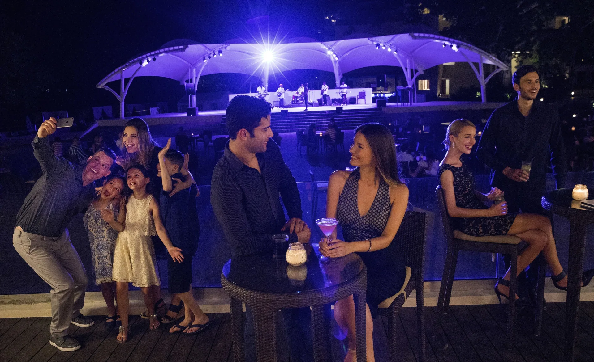 Guests enjoy drinks with a lit outdoor stage in the background at Royalton Negril.