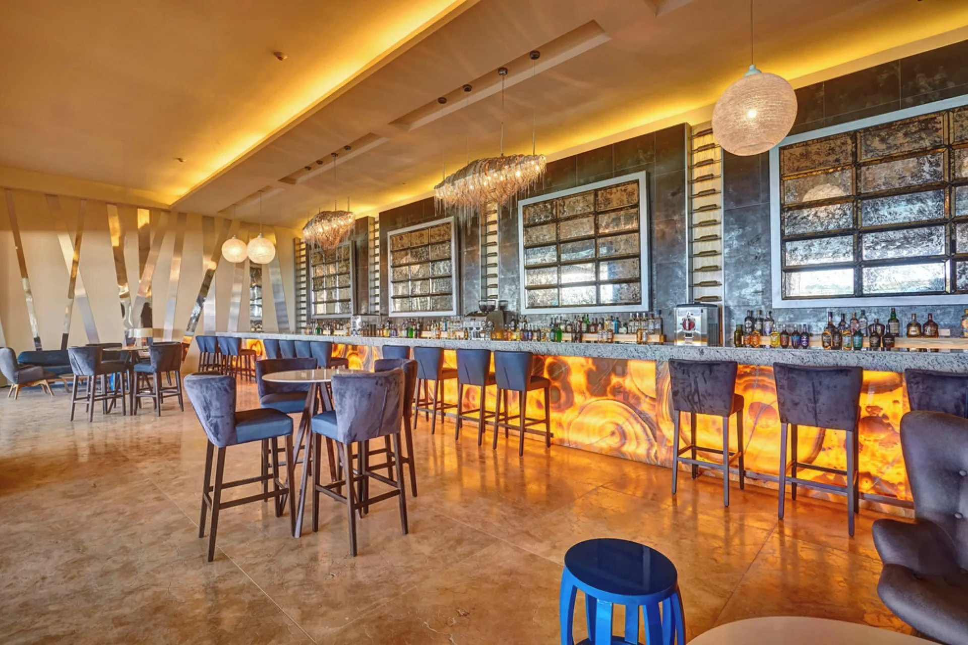 Lobby bar with blue chairs, illuminated counter and pendant lighting at Royalton Negril.