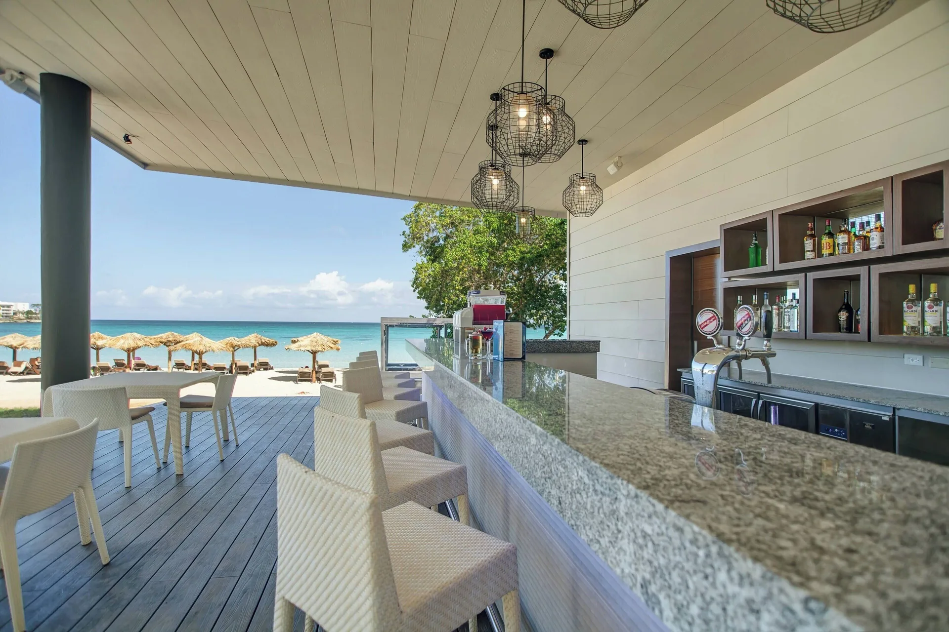 Beachfront bar with white stools and ocean views at Royalton Negril.