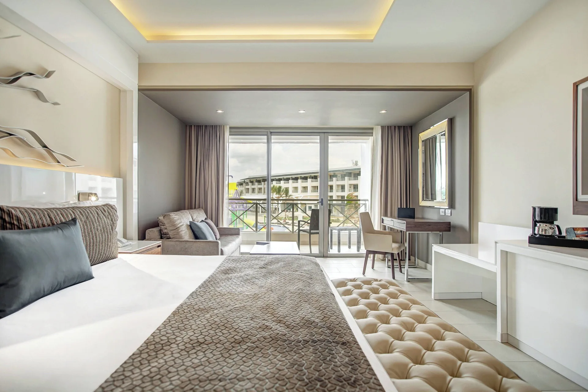 Luxury Junior Suite king bed with bench, sofa, desk, and balcony at Royalton Negril.