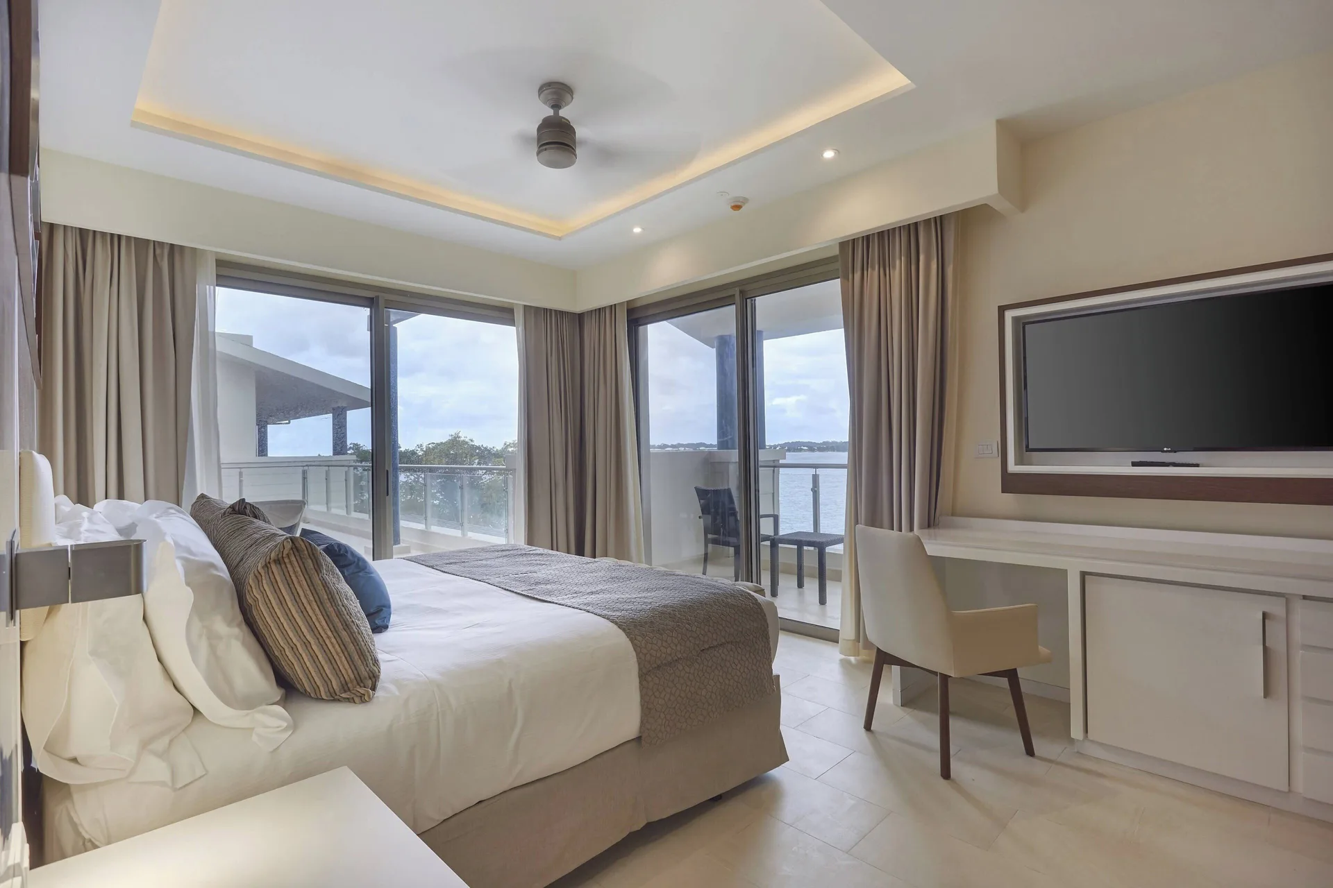 King bedroom with desk, wall TV and balcony views at Royalton Negril.