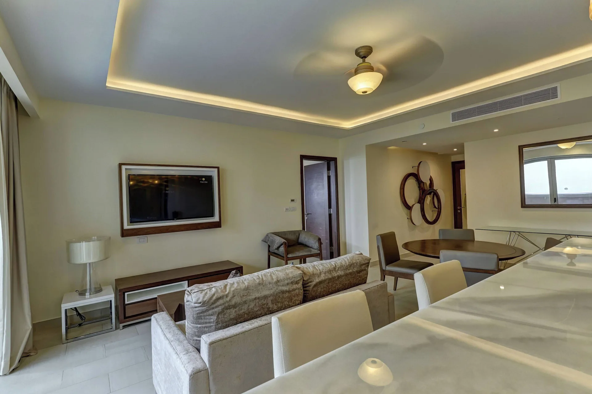Penthouse lounge with sofa, wall TV, dining table and bar counter at Royalton Negril.