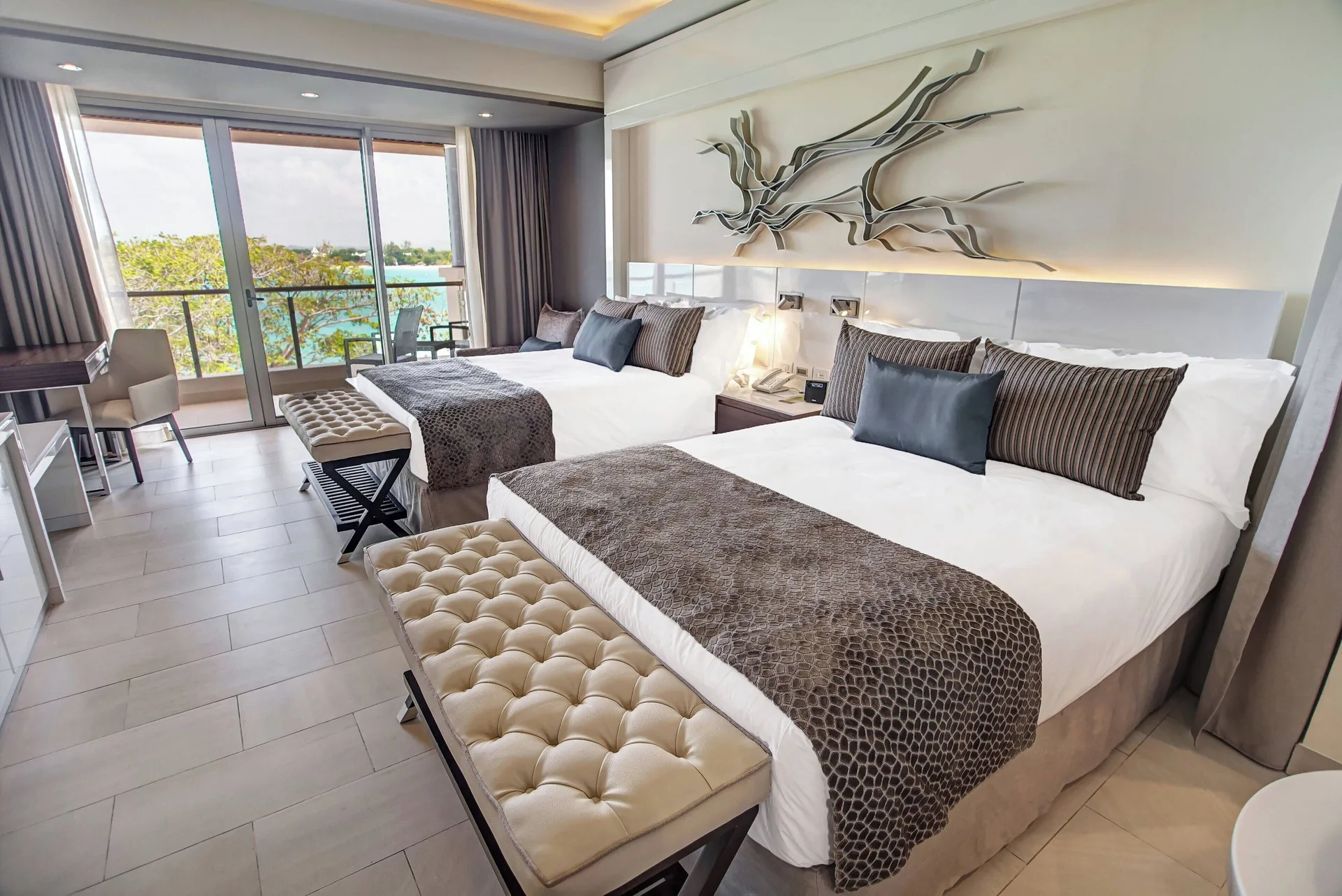 Two beds and balcony doors with ocean visible in a Royalton Negril suite bedroom.