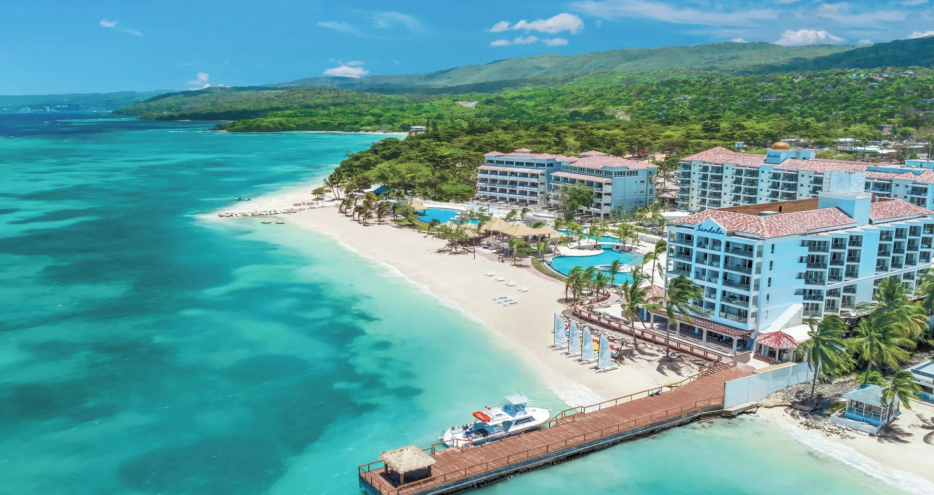 Aerial view of the beach, pier, pools, and resort buildings at Sandals Dunns River.